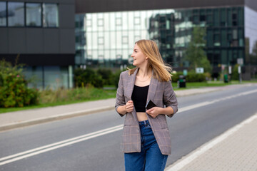 Portrait of young happy blond woman with phone walking on the street in the city. Technology or people concept