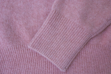 Pastel pink sweater sleeve with cuff as background. Knitted wool and cashmere sweater. Warm and fashionable clothes. Comfortable style cloth. Cozy composition. Soft focus