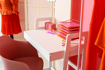 Stylist's workplace with notebooks and folding screen near pink wall
