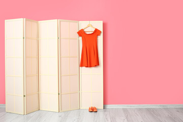 Light folding screen with red dress and shoes near pink wall