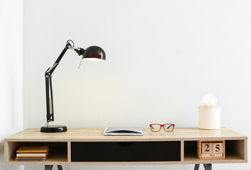 Black lamp with notebook and eyeglasses on desk near light wall