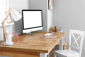 Modern workplace with blank computer screen near light wall