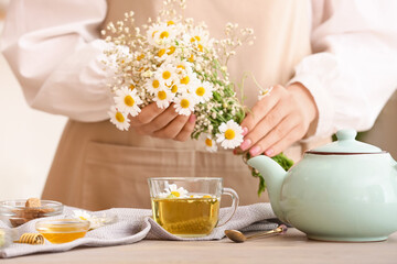 Woman with chamomile flowers, teapot and cup of tea on table
