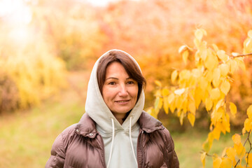 Portrait of a cute woman in a hoodie outdoors on the background of an autumn park
