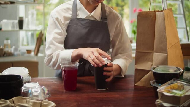 Food delivery service. Woman closing plastic glass with drink and paper cup with coffee to go. Preparing take away meals. Healthy eating habits. Online contactless food shopping.