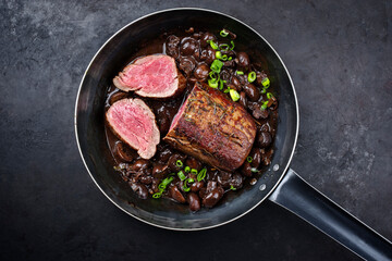 Traditionelles gebratenes Dry Aged Angus Rinderfilet und Medaillon natur mit Champignons in Rotweinsoße serviert als close-up in einer klassischen Bratpfanne