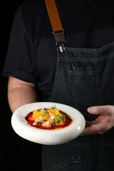 chef hold ceramic plate with salmon tartar on black background