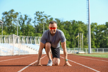 Sporty mature man getting ready to run at stadium