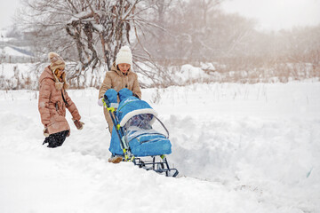 Fototapeta na wymiar young woman with baby stroller and her daughter walk in the park in snowfall in winter