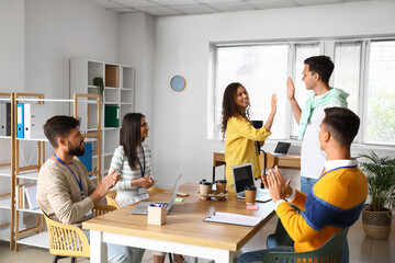 Young business co-workers giving each other high-five after presentation in office