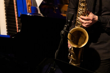 Obraz premium A tenor saxophone player dressed all in black from of a big band section playing a solo in front of a microphone during a live concert