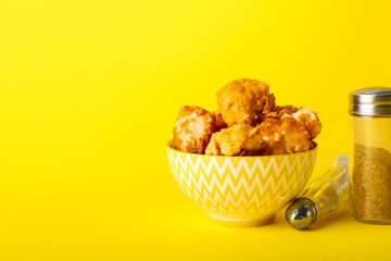 Bowl with tasty fried popcorn chicken and spices on yellow background