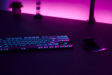 Low light scene of computer input devices, pink illuminated wall in background.