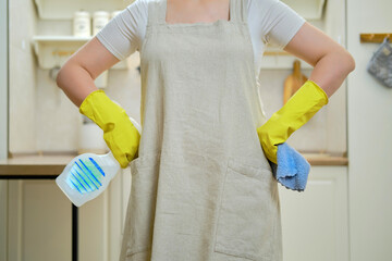 A woman with a rag and a bottle of detergent is preparing for cleaning in the home kitchen