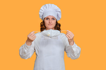 Woman chef with medical face mask on yellow studio background, mockup copy space. Concept of ending...