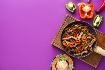 Frying pan with tasty beef Fajita and sombrero hat on purple background