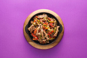 Frying pan with tasty beef Fajita on purple background