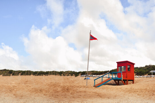 Red wooden cabin on the beach for coastguard. Coast guard cabin in Ostende (coast Argentina). Dangerous sea flag on a sunny beach day