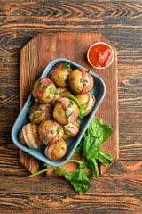 Baking dish of tasty baked potatoes with bacon on wooden background