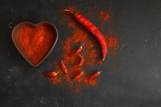 red hot chili peppers  powder in heart shaped bowl on black stone table. Love concept. Top view flat lay with copy space