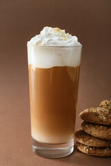 Glass of tasty latte with nuts and cookies on brown background