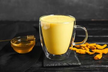Glass cup of healthy turmeric latte with honey on dark wooden table, closeup