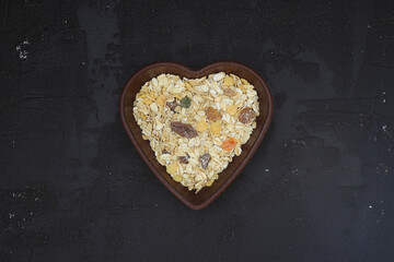 Oatmeal flakes and oats on a heart shaped plate on black background. Healthy breakfast. Organic and vegetarian food. Porridge and cereal concept. Flat lay, copy space for text