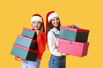 Beautiful young women with Christmas gifts on yellow background