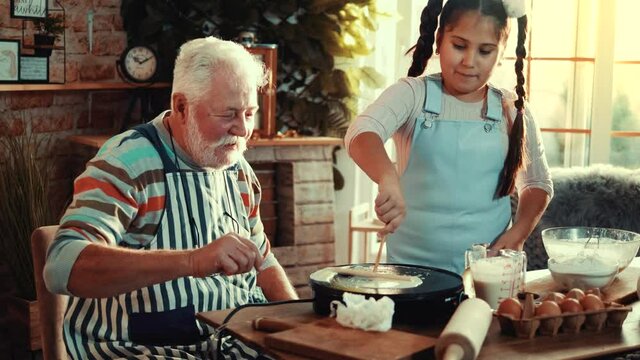 Senior man learning granddaughter how to frying crepe on crepe maker
