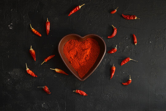red hot chili peppers  powder in heart shaped bowl on black stone table. Love concept. Top view flat lay with copy space