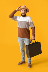 Handsome man with Black Friday shopping bag on yellow background