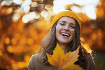 Naklejka na ściany i meble smiling modern woman in brown coat and yellow hat