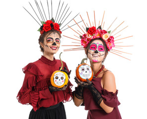 Stylish women with painted skull on faces and pumpkins against white background. Celebration of Mexico's Day of the Dead (El Dia de Muertos)
