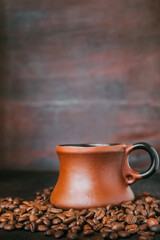 Brown earthenware coffee cup on a wooden table. Roasted coffee beans lie around the cup. Copy space