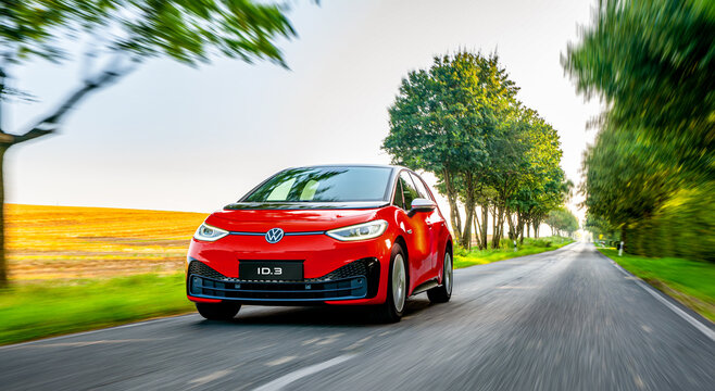 The Volkswagen VW ID.3 Electric Compact Car Driving On A Road At Sunset With Modern Urban Background - Motion Blur Chasing Shot