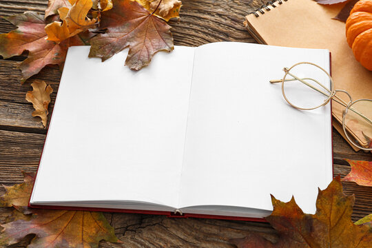 Blank open book, eyeglasses and autumn leaves on wooden background