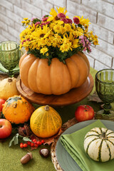 Beautiful bouquet of autumn flowers in pumpkin on served table near brick wall