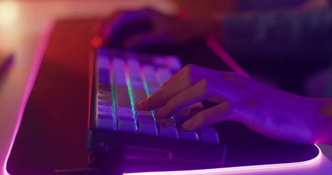 Close-up hands shot asia guy gamer use keyboard and mouse controller play video game with neon light computer in desk at home. Online esport streaming game online, Home quarantine activity concept.