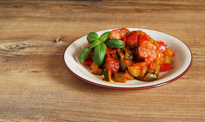 close-up of vegetable stew, eggplant, onion, zucchini with tomato sauce, garlic and herbs in a bowl on a wooden table, landscape view from above