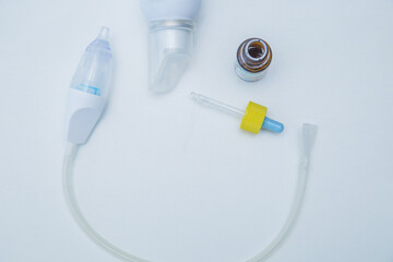The children's aspirator lies in a semicircle on a white background, to the side of it are drops from a runny nose with a pipette and water for washing. High quality photo