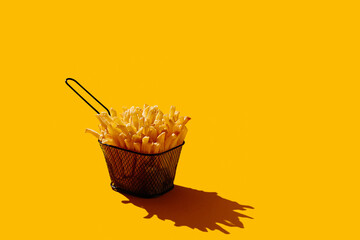 French fries in fryer basket on yellow pastel background