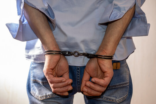 A man handcuffed on a light background. Concept: a detained criminal, an illegal migrant in a police station, a border violator, a bribe taker and a corrupt official, arrest.