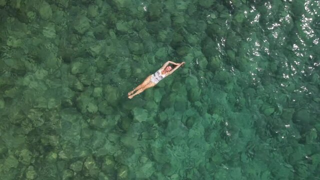 woman in a white swimsuit swims on her back in the Mediterranean Sea. Blue color of water
