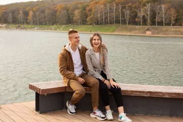 a young handsome guy hugs a young beautiful girl by the shoulders on the pier of the city river autumn Park