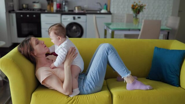 happy Mother and joyful baby at home. Happy caucasian mother playing with infant child girl standing at home on yellow safa.