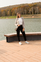 a young beautiful girl in a gray jacket stands on the pier of the river autumn city park