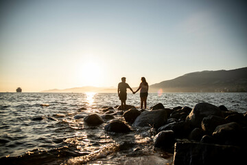 a young couple holding hands at sunset in front of the ocean