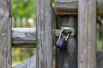 The padlock locked on a gate in a wooden fence.