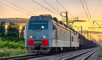 Obraz na płótnie Canvas Electric locomotive hauling a cargo train at sunset
