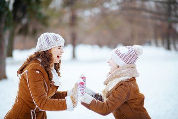 smiling mom and child playing outside in city park in winter